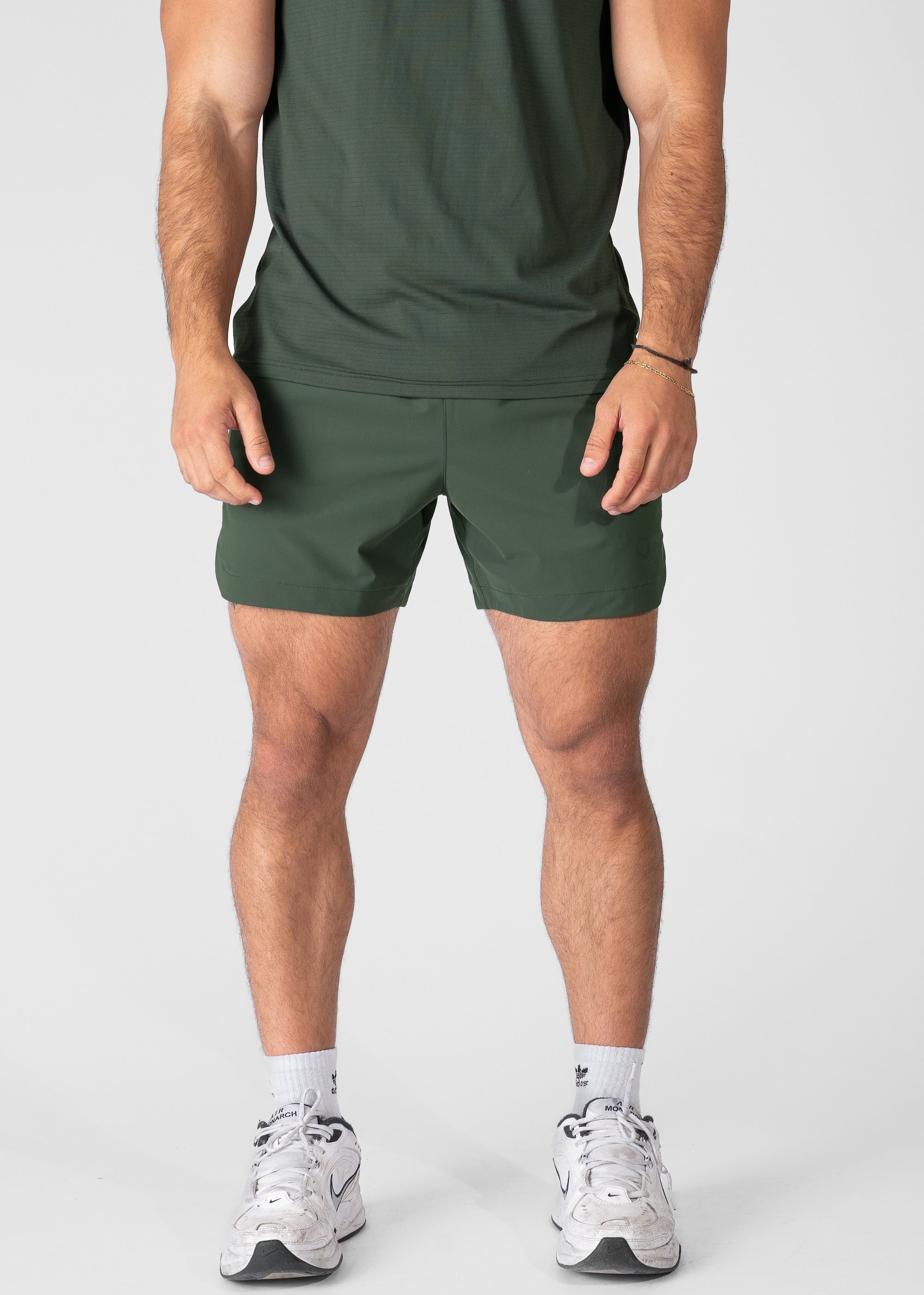 Man wearing dark green hybrid shorts on plain background. #color_dark green #model_A