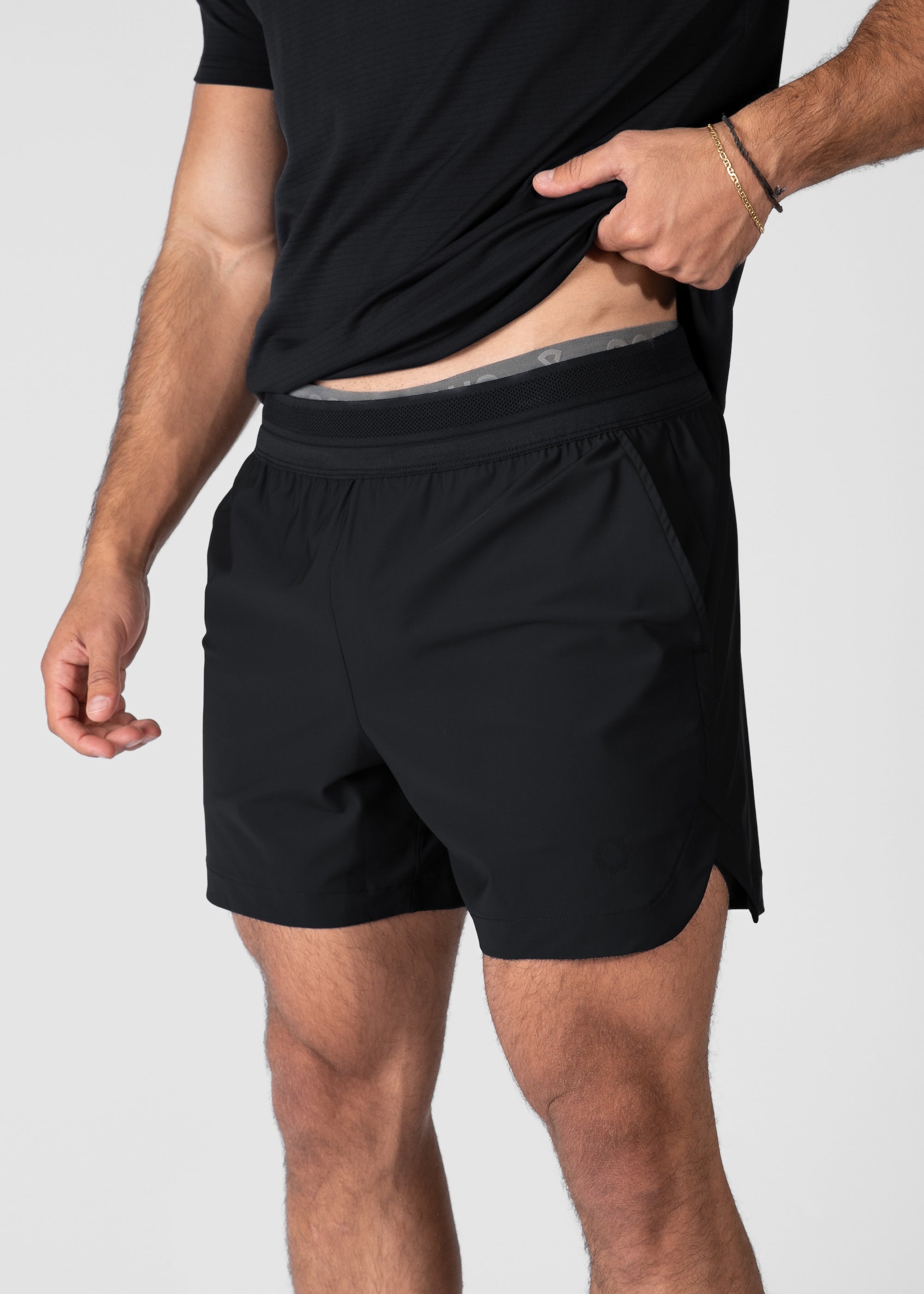 Man wearing black hybrid shorts lifting shirt to reveal waistband. #color_black