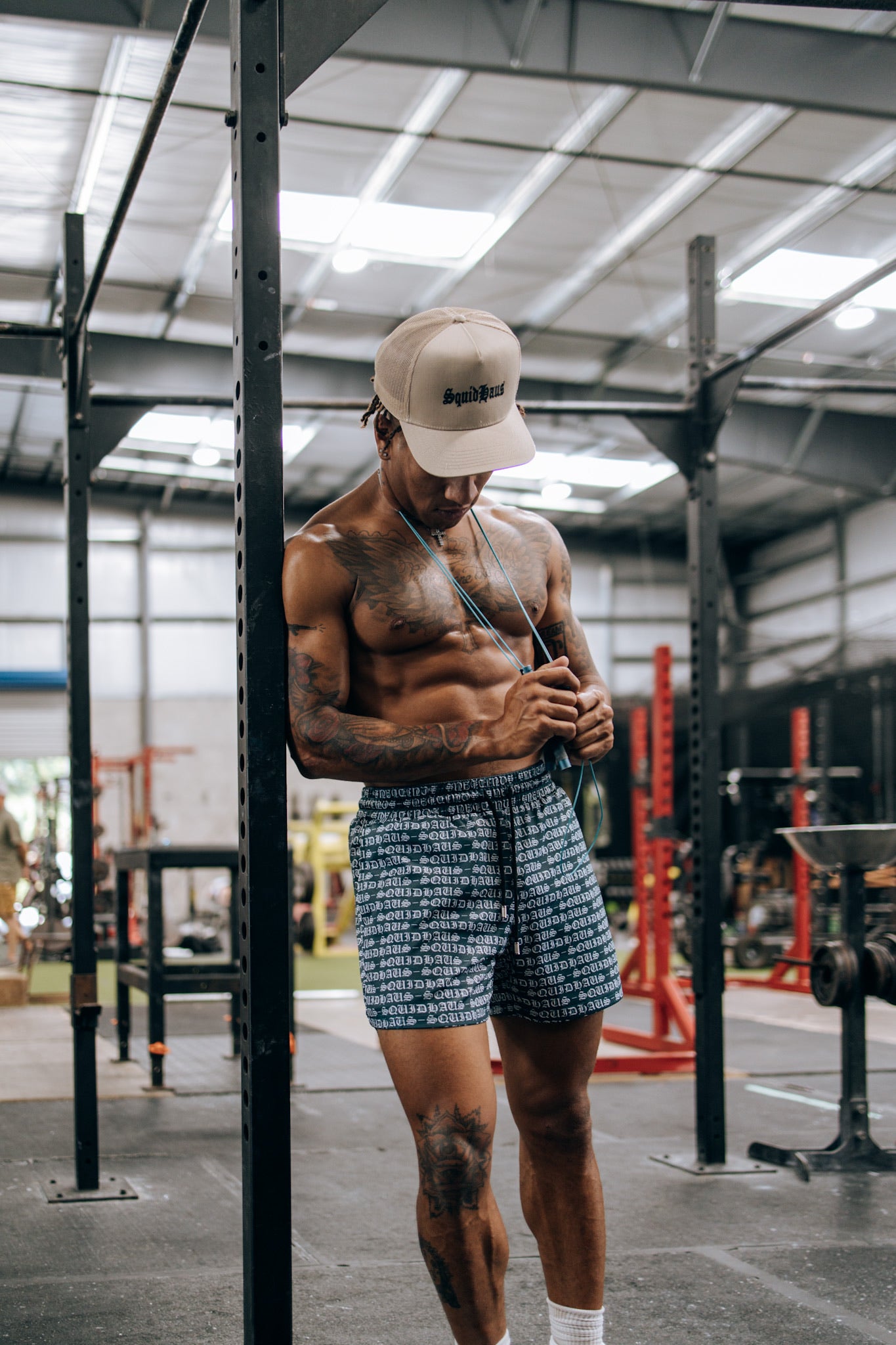An athlete leans against a pole at the gym with a jump rope slung over his sholder