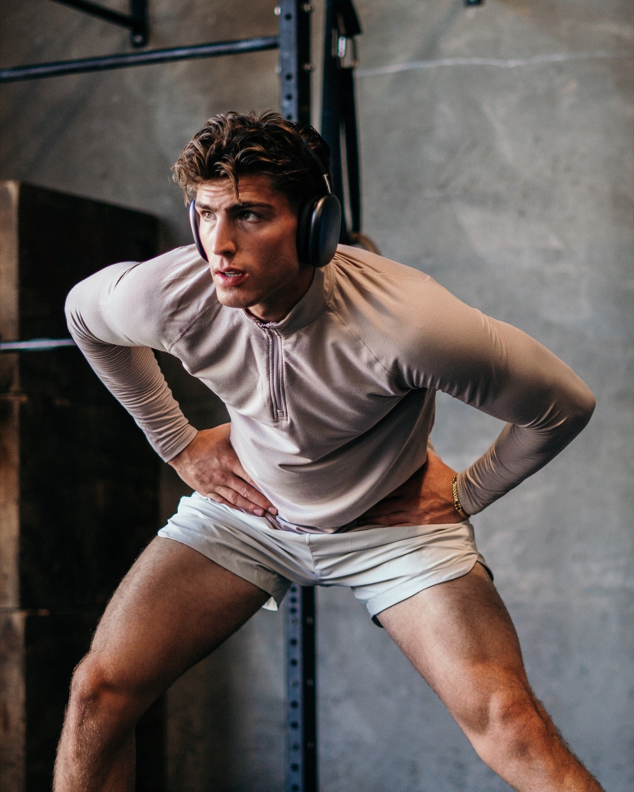 Athlete in a stone Haus quarter zip and white shorts catching his breath at a squat rack