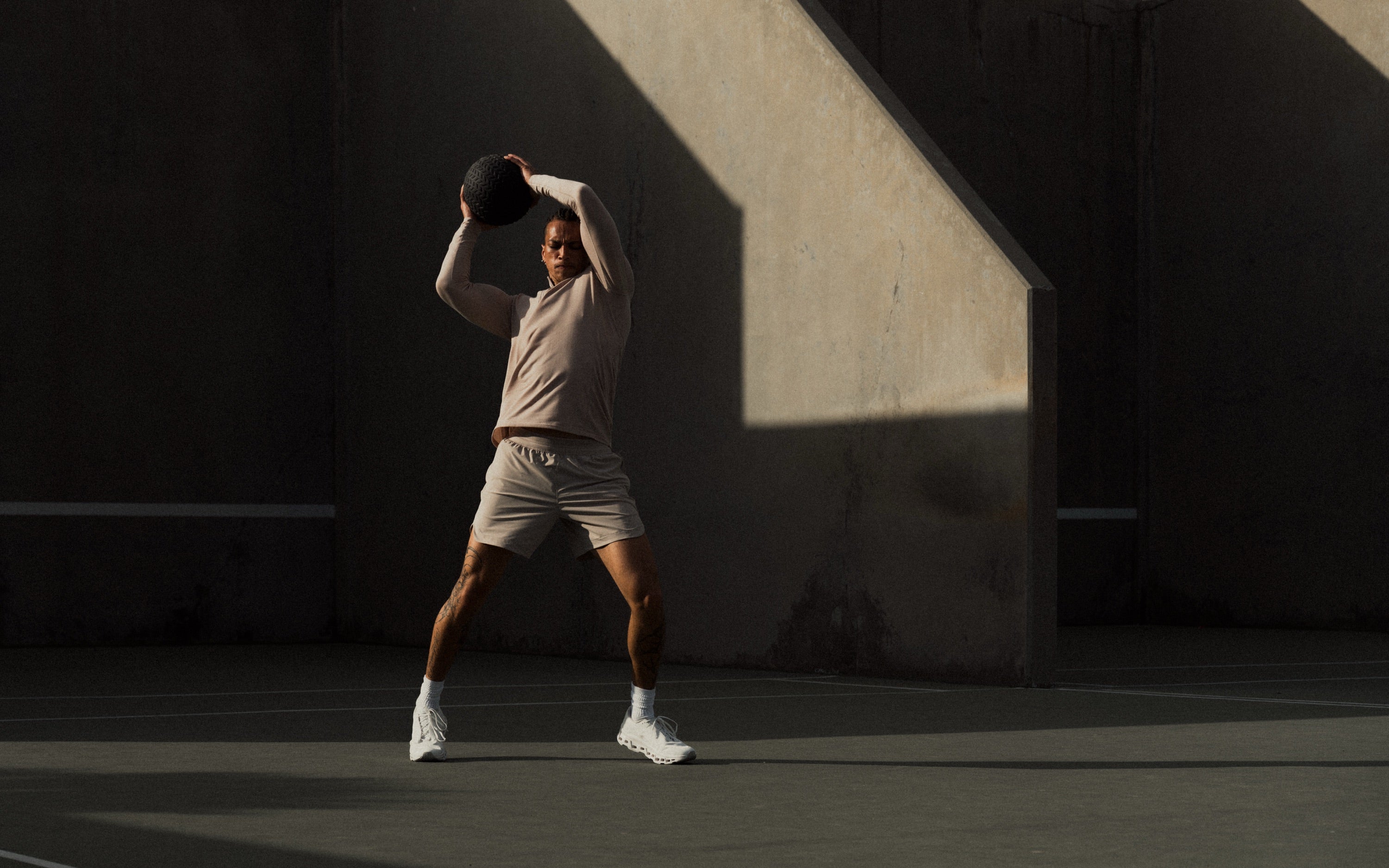 Athlete in a sand Haus training set swinging a medicine ball overhead on a sunlit court