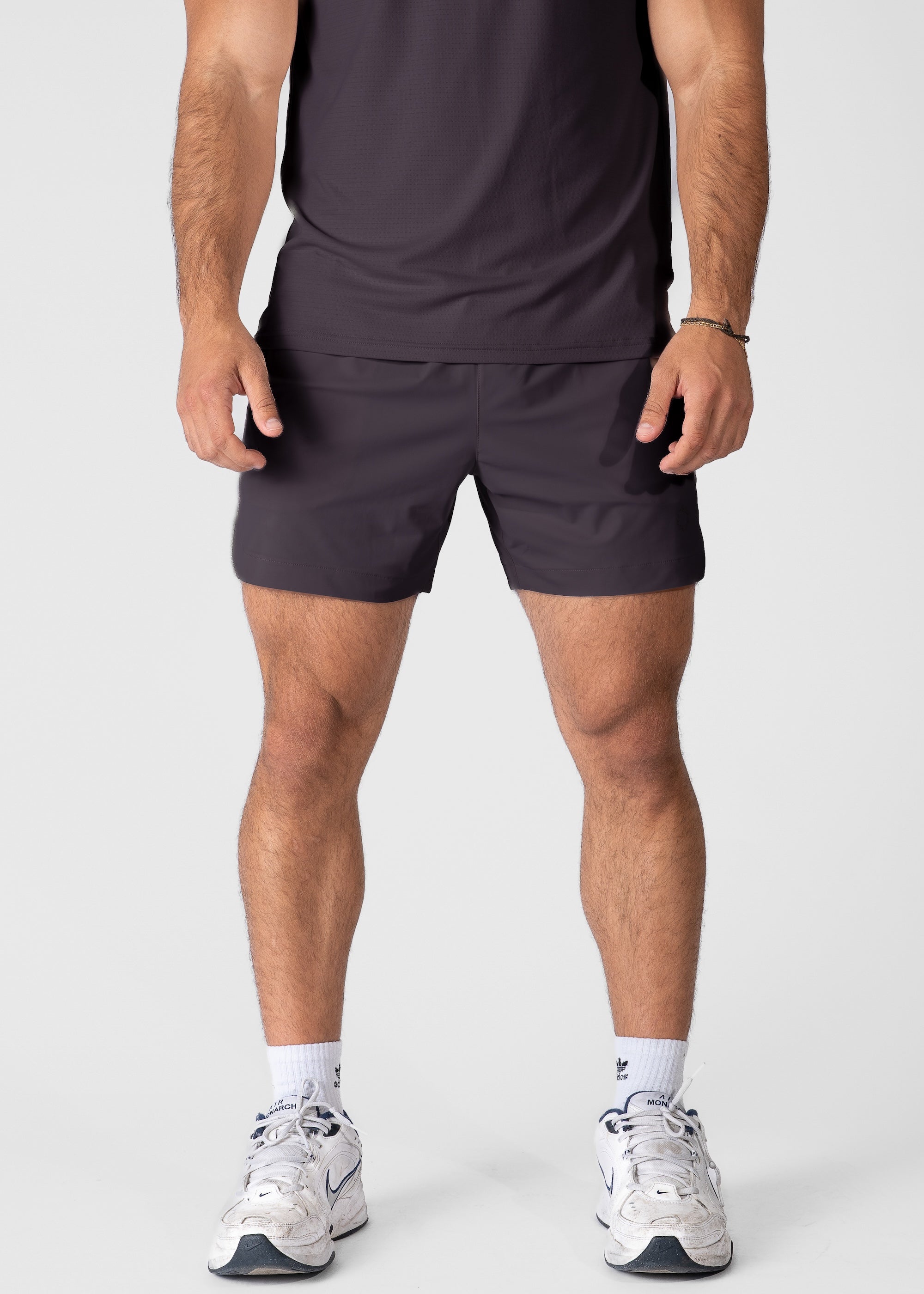 Man wearing dark purple hybrid shorts on plain background. #color_dark purple #model_A