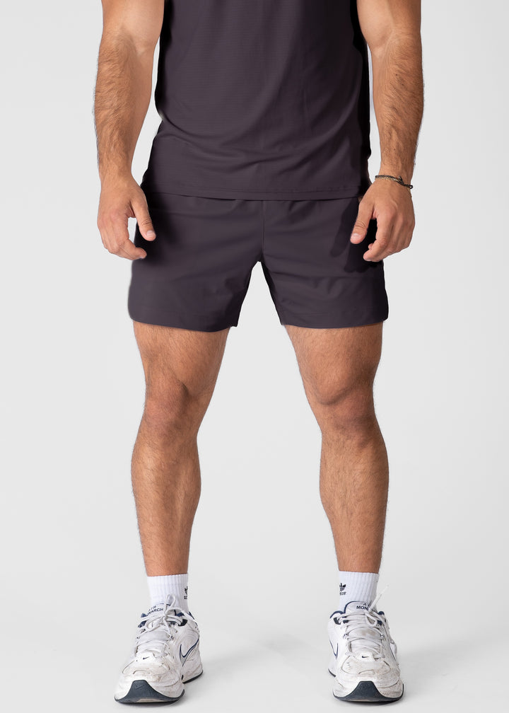 Man wearing dark purple hybrid shorts on plain background. #color_dark purple #model_A