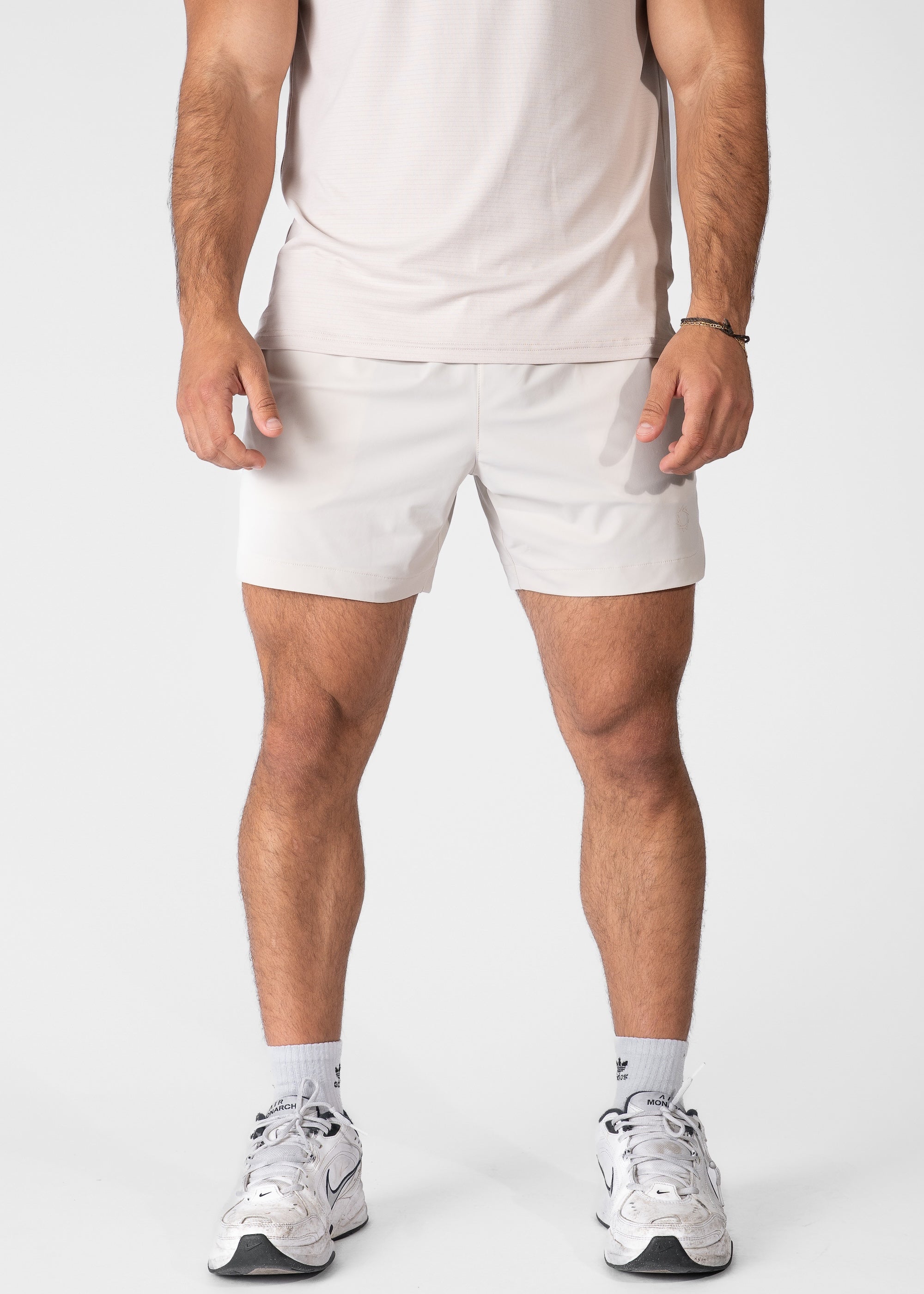 Man wearing light beige hybrid shorts on plain background. #color_sand #model_A