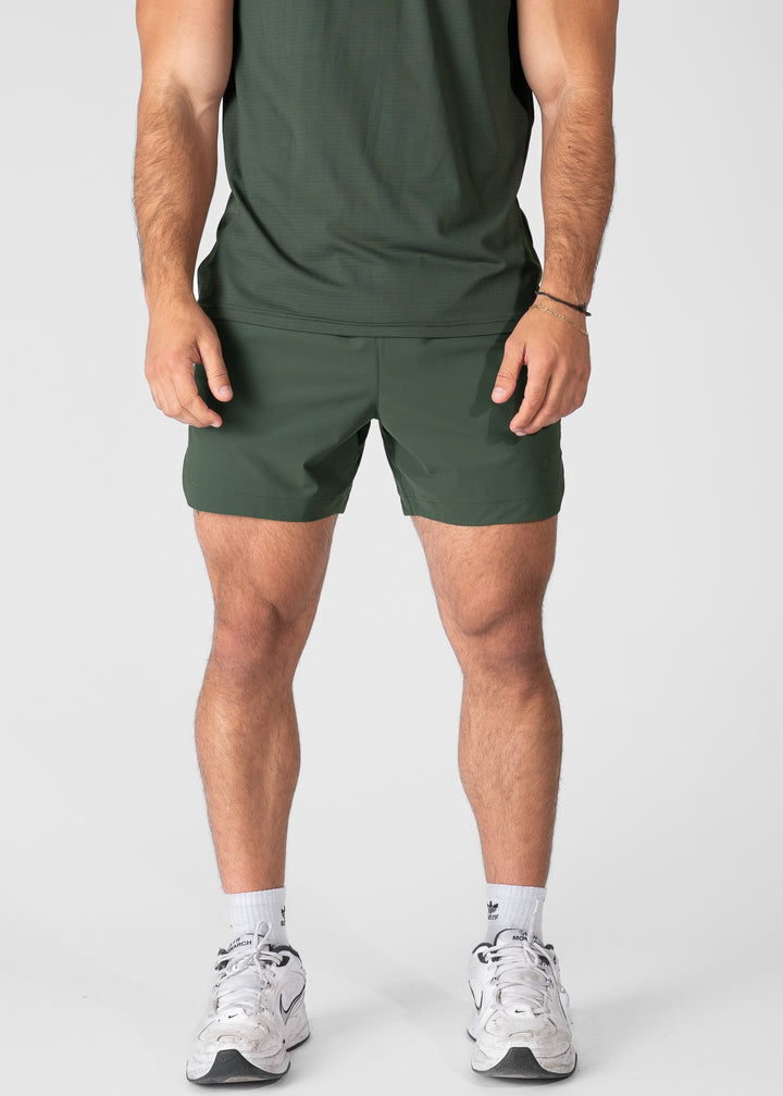 Man wearing dark green hybrid shorts on plain background. #color_dark green #model_A