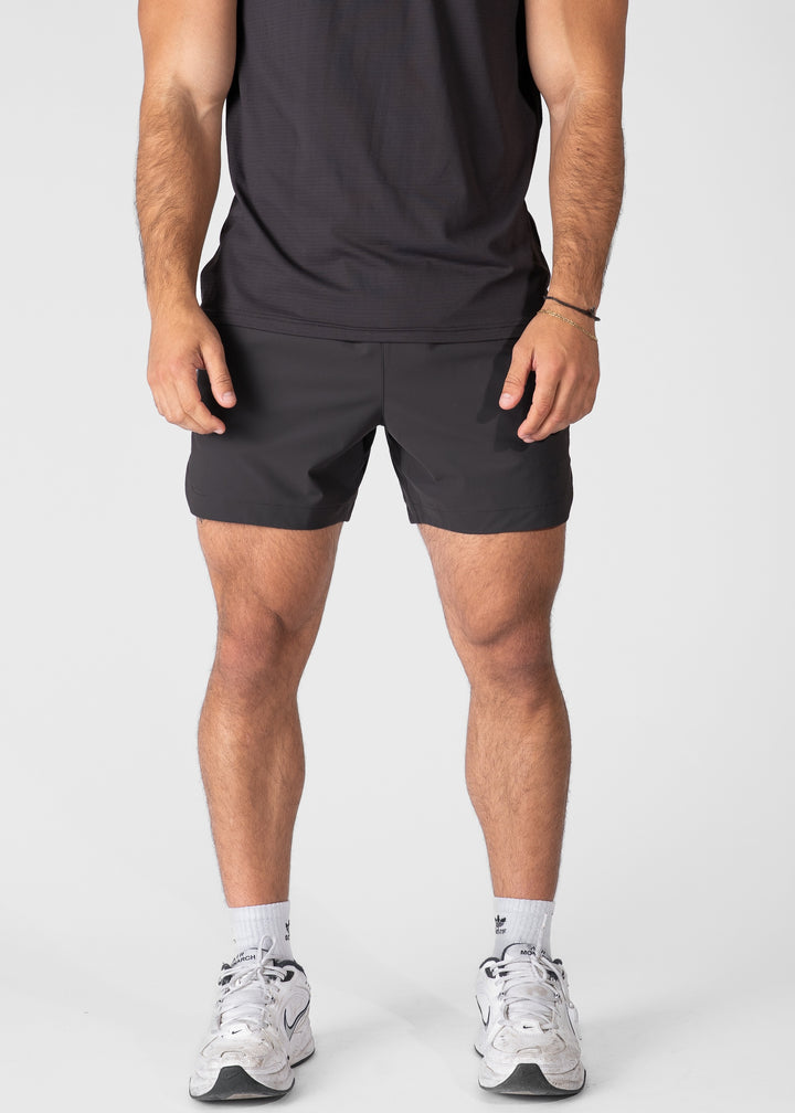 Man wearing dark grey hybrid shorts on plain background. #color_charcoal grey #model_A