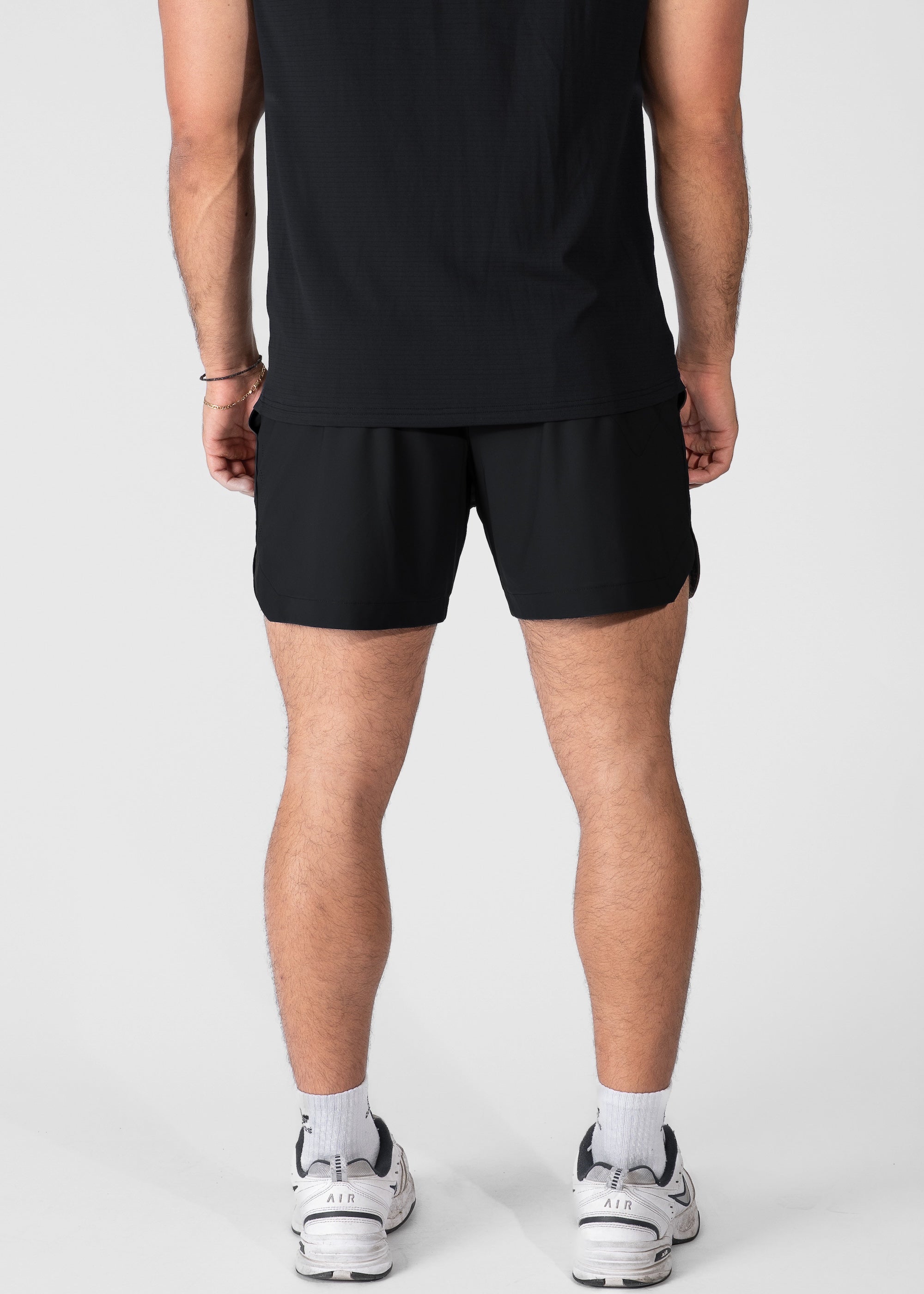Rear facing shot of a man wearing black hybrid shorts #color_black