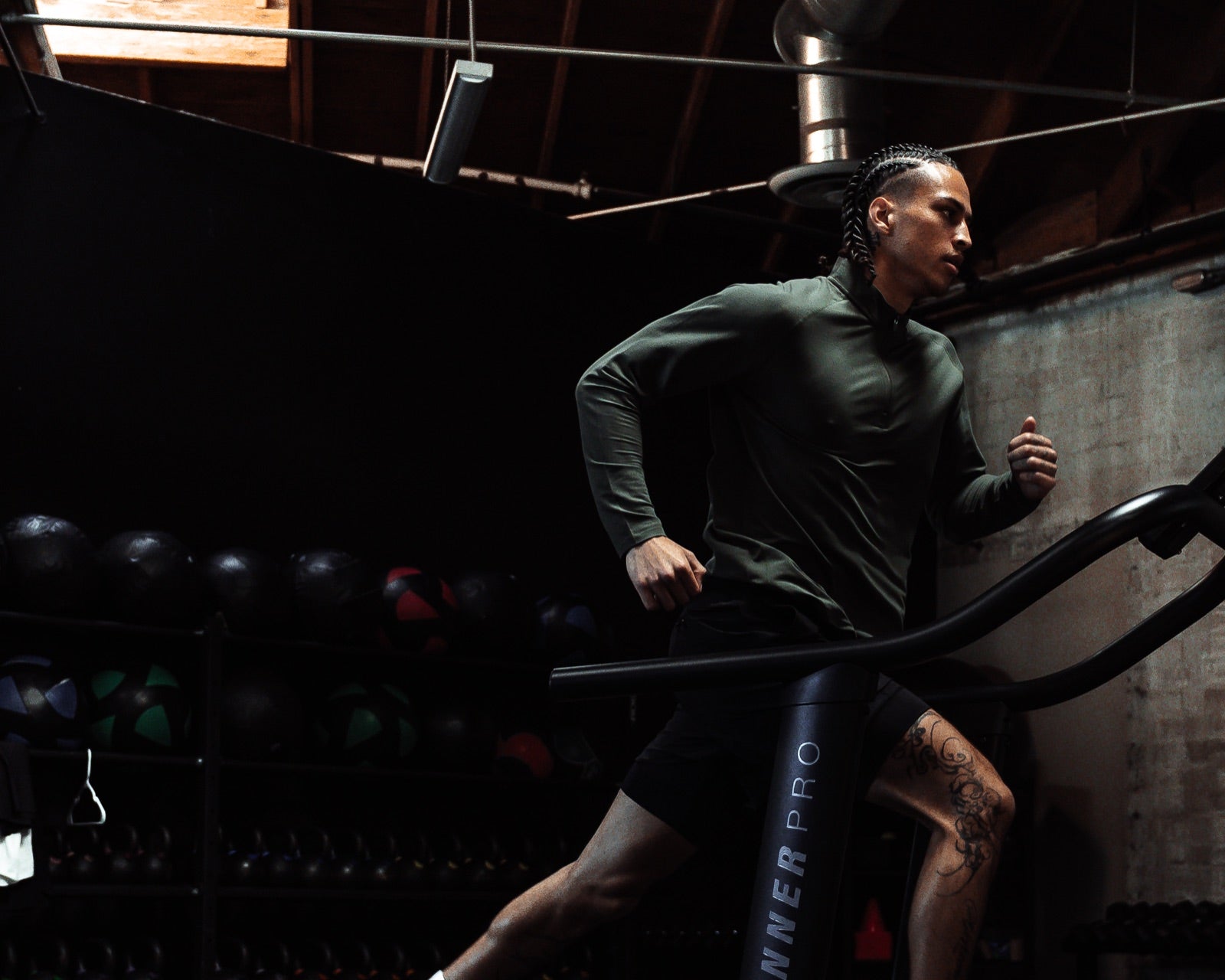 Athlete in a green Haus quarter zip running on a curved treadmill in a dim gym