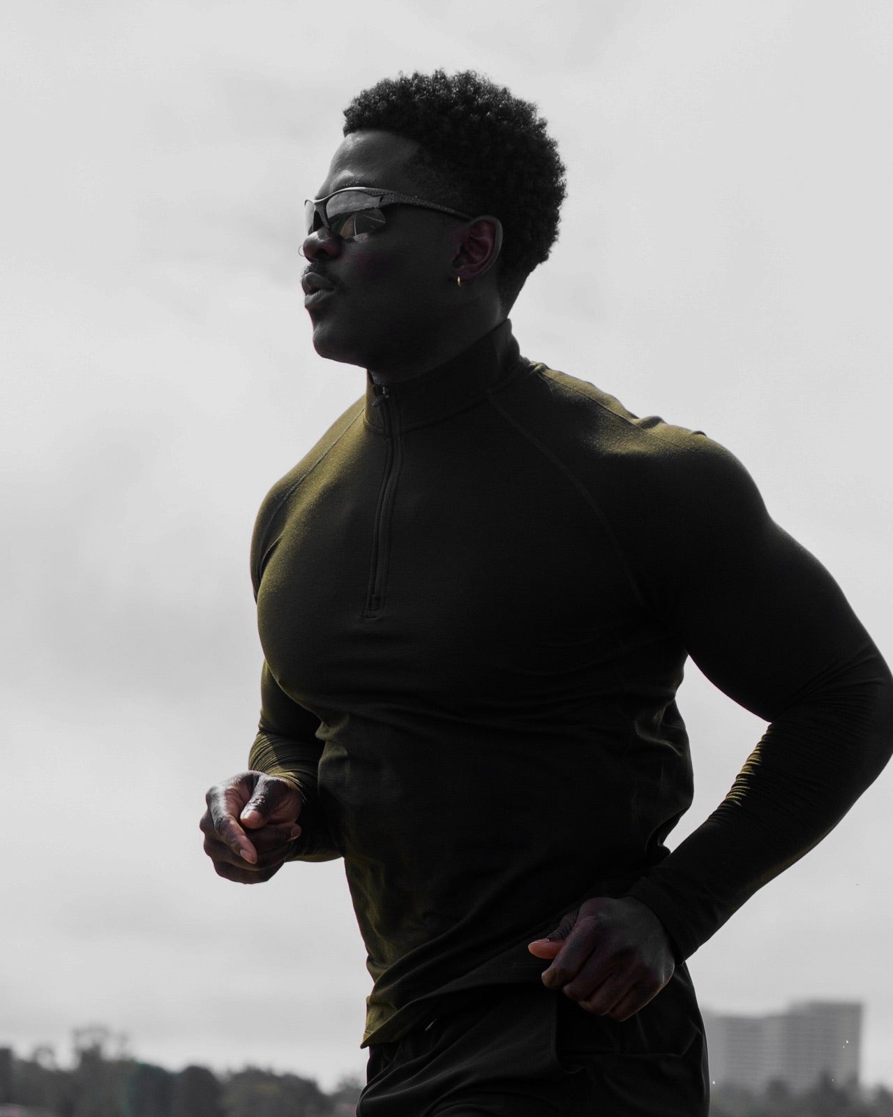 Runner in an olive Haus quarter zip and sunglasses under an overcast sky
