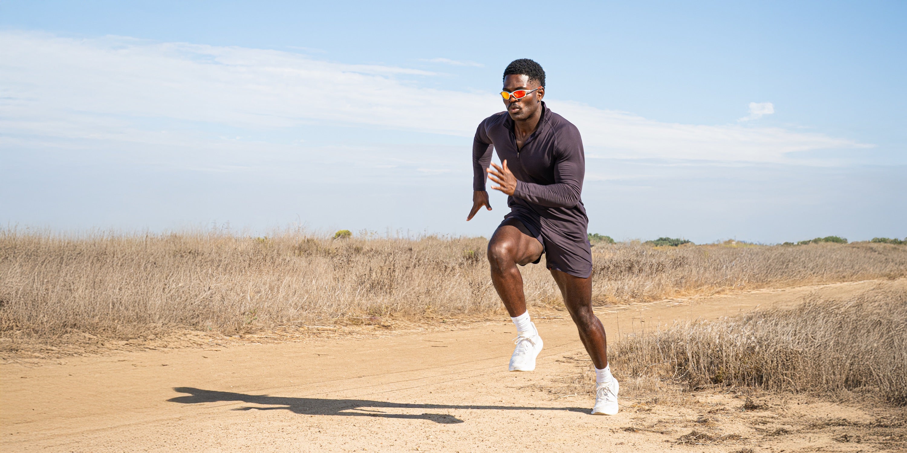 Runner in a plum Haus long sleeve and shorts on a dirt coastal trail