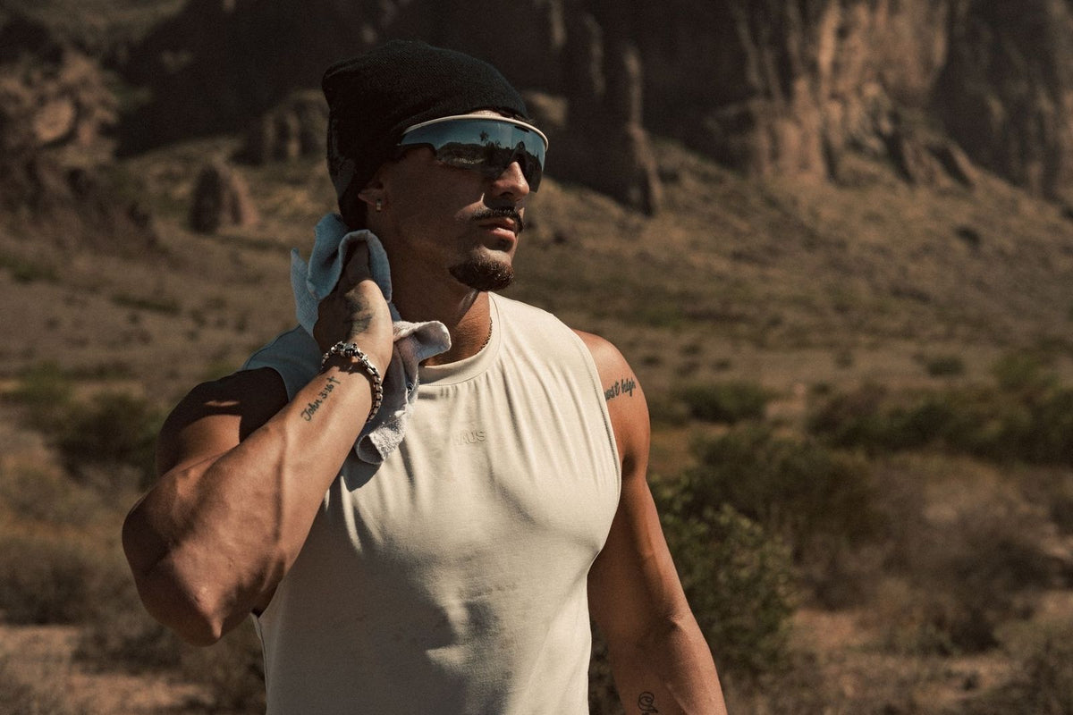 Haus athlete in the desert wiping sweat with a towel, wearing a cream Haus tank, beanie and shield sunglasses